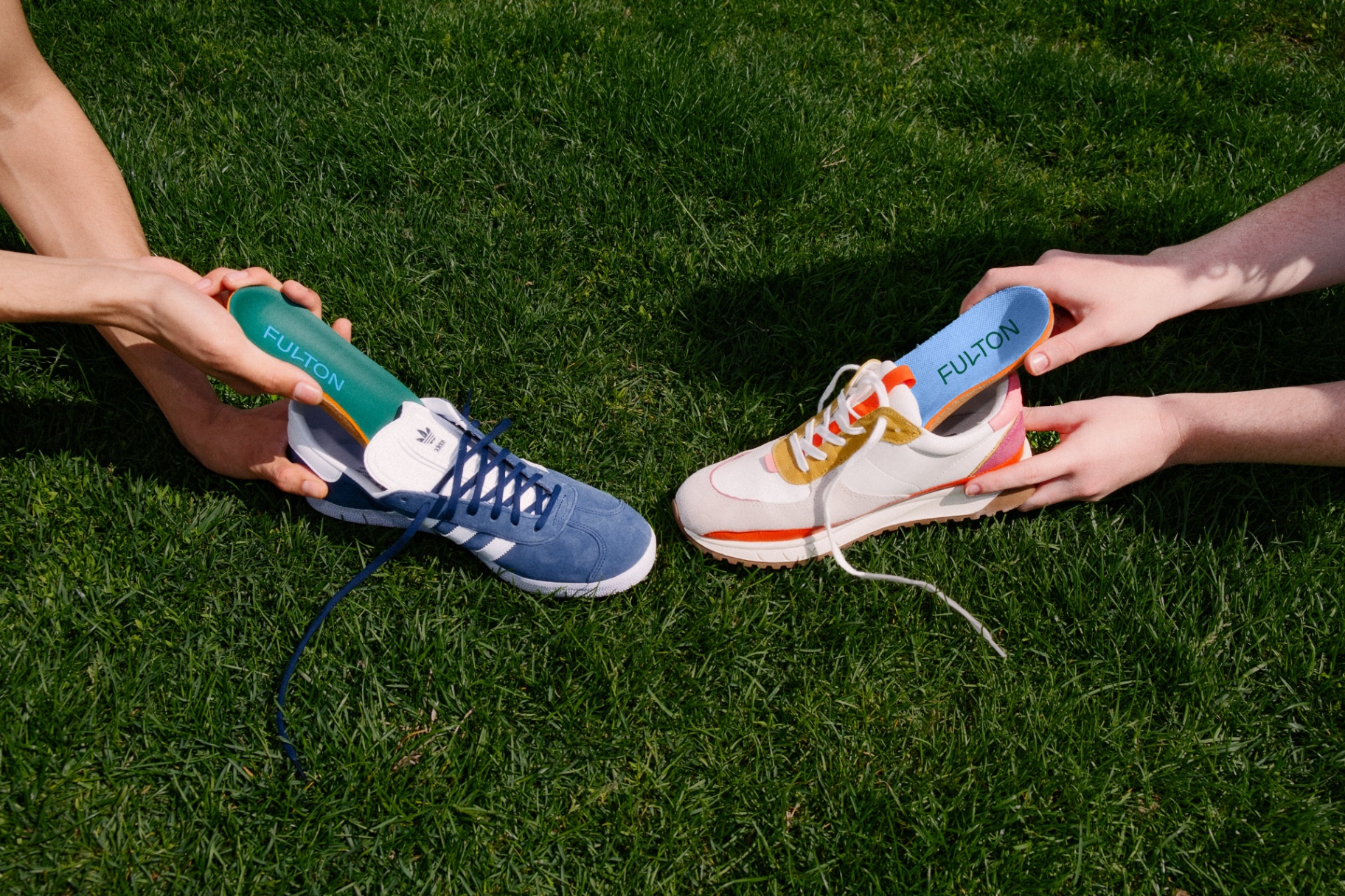 Hands holding Fulton insoles above sneakers on grass